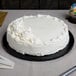 A white cake with white frosting on a black round cake board.