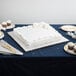 A white cake with silver decorations on a silver cake drum on a table.