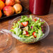 A clear plastic bowl of salad with green leaf lettuce, strawberries, cheese, apples, and oranges.