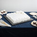 A white square cake on a black Enjay cake drum on a table.