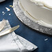 A white cake on a black Enjay round cake board with silverware on a table.