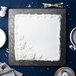 A white square cake on a black Enjay cake board with white frosting and flowers.