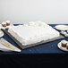 A white cake with black square cake drum on a table.
