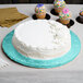 A white round cake on a blue Enjay cake drum with cupcakes on the table.