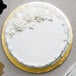 A white cake with white frosting and flowers on a gold Enjay round cake drum on a table.