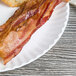 A white 9" coated paper plate with bacon and hash browns on it.