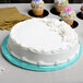 A white cake with blue frosting on a blue Enjay cake drum on a table.