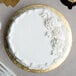 A white cake with frosting on a gold Enjay round cake board.