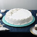 A white cake on a blue Enjay round cake drum on a table.