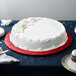 A white cake on a red Enjay round cake drum on a table.