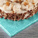 A cake with frosting and pecans on a blue Enjay square cake drum on a table in a bakery display.