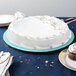 A white cake on a blue Enjay round cake drum on a table.