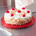 A cake with whipped cream and cherries on a red Enjay cake board.