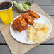 A white paper plate with fried chicken, chips, and a drink.
