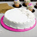 A white cake with pink frosting on a pink Enjay round cake board on a table.