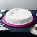 A white cake with pink frosting on a pink Enjay cake board on a table.