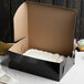 A black Enjay 1/4 sheet cake box with a white frosted cake inside.