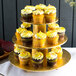 An Enjay gold cupcake stand holding cupcakes with yellow frosting and sprinkles.