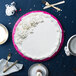 A cake with white frosting on a pink Enjay cake drum on a blue table.