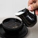 A person pouring milk into a black American Metalcraft porcelain bell creamer.