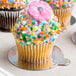 A close-up of a cupcake with sprinkles and a pink flower on top on an Enjay round single serve dessert board.