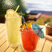 Two glasses of yellow drinks with straws and umbrellas on a table.