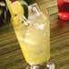 A glass of ice and lemonade on a table with a straw.