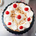 A cake with white frosting and red cherries on a black Enjay cake circle.