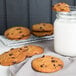 Preformed David's Cookies chocolate chip cookie next to a glass of milk.