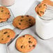 A glass jar of David's Cookies chocolate chip cookies with a glass of milk.