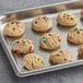 Preformed David's Cookies M&M's cookie dough on a baking sheet with cookies topped with M&M's.