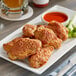 A plate of Brakebush breaded chicken wings with celery, dip, and red sauce.