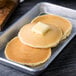 A Krusteaz buttermilk pancake with butter on top on a metal tray.