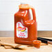 A jug of Texas Pete hot sauce on a cutting board next to a glass of hot sauce.