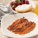 A plate of Hatfield sliced bacon with a bagel and strawberries and a glass of juice.