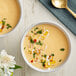 Two bowls of LeGout cream soup with green herbs and white sauce served with a gold spoon and a flower on a blue cloth.