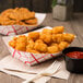 A bowl of Ore-Ida Golden Tater Tots with a plastic fork and ketchup on a table.