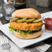 A Brakebush chicken sandwich with pickles and ketchup on a white plate.