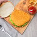 A hand holding a fried chicken sandwich with fries and ketchup on a wooden board.