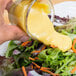 A hand pouring Ken's Golden Honey Mustard Dressing over a salad.