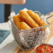 A basket of Fry Foods 3" Breaded Mozzarella Cheese Sticks with a bowl of red sauce.