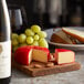 A Castello Gouda cheese wheel and grapes on a cutting board.