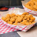 Two baskets filled with Brakebush popcorn chicken nuggets with ketchup on a table.