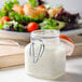 A Ken's Foods jar of white liquid Buttermilk Ranch dressing next to a bowl of salad.