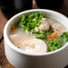 A bowl of soup with shrimp and vegetables next to a tub of Minor's Crab Base.