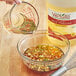A hand pouring 1 gallon of seasoned rice wine vinegar into a bowl of food.