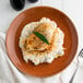 A plate with a split boneless skinless chicken breast and mashed potatoes on a white surface with a leaf on top.