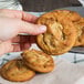 A hand holding a David's Cookies peanut butter cookie.