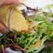 A hand pouring Gulden's Spicy Brown Mustard over a salad on a table.