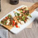 A slice of pizza with Hormel beef pizza topping, meat, and vegetables on a wooden board.